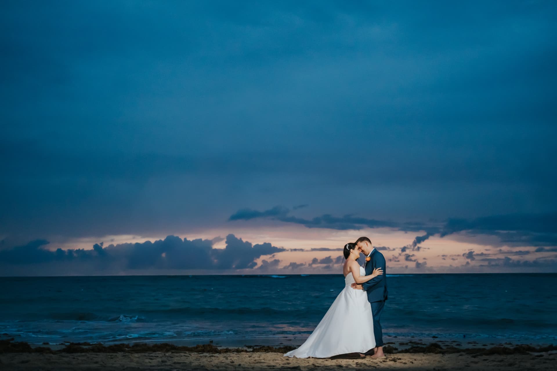 Bride and groom on a Punta Cana beach beneath a dramatic sky at dusk