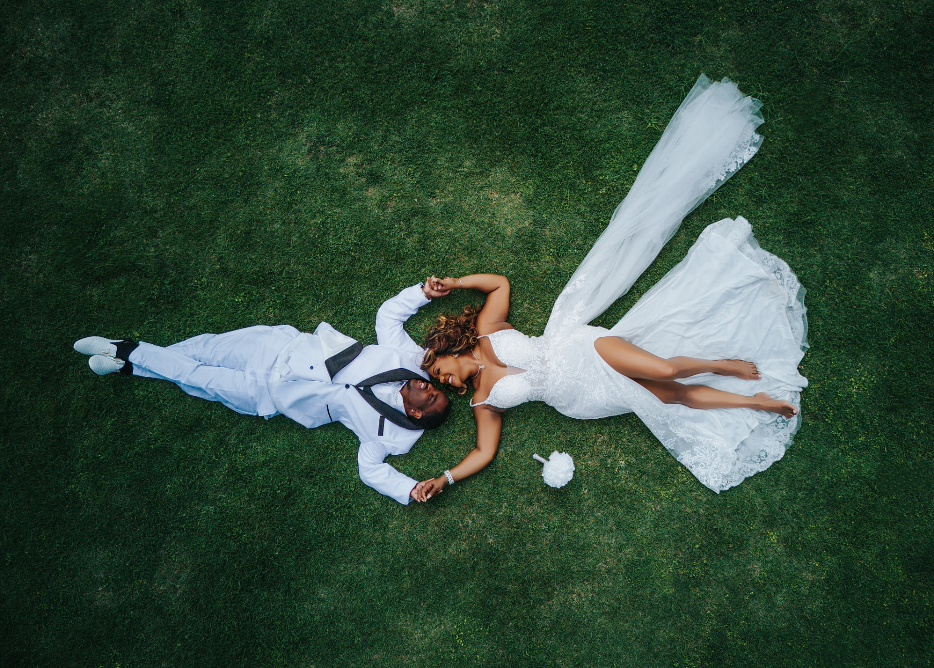 Aerial photograph of a bride and groom lying side by side on green grass