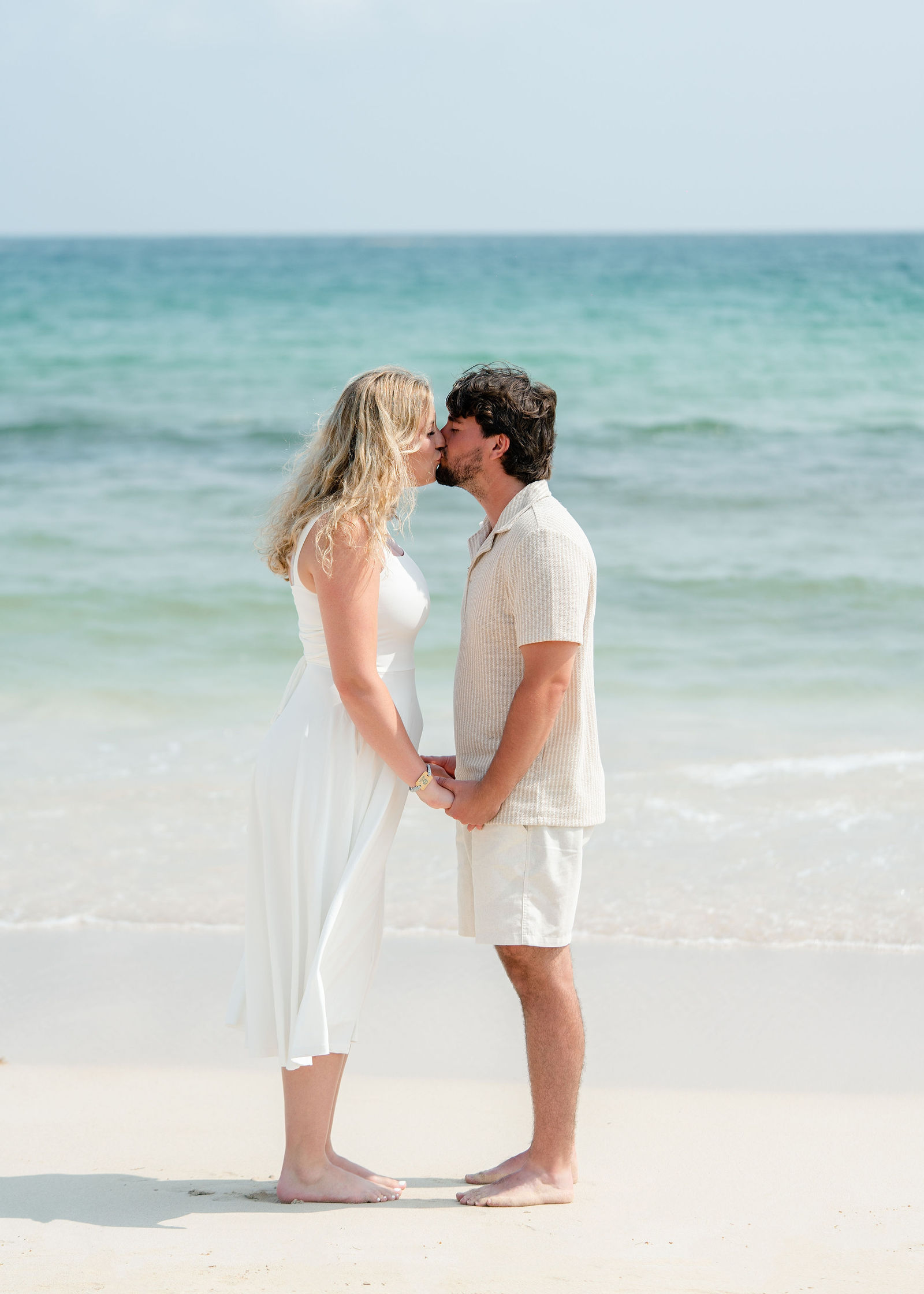 Newly engaged couple kissing barefoot at the shoreline